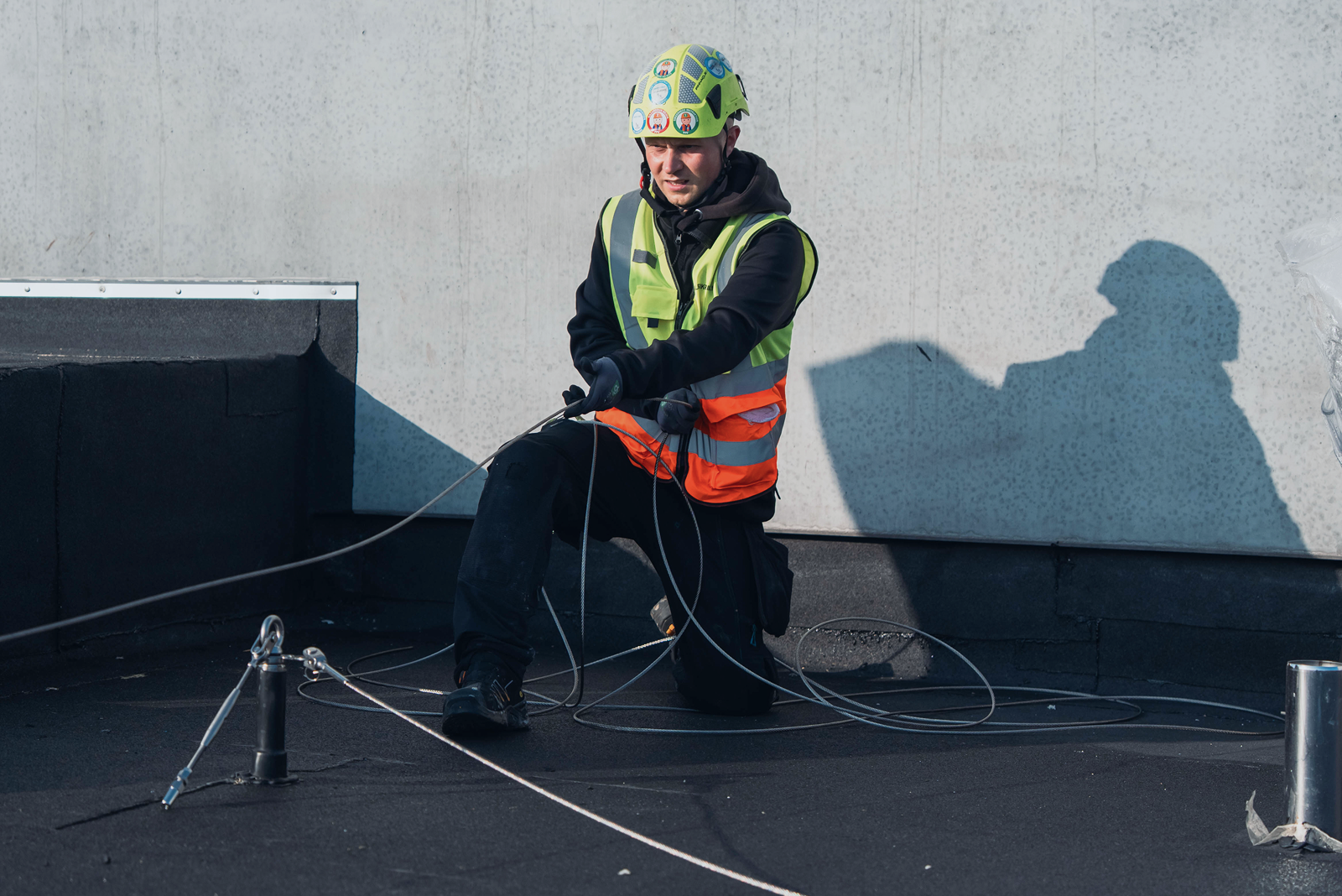 Montør arbejder med wirebaseret faldsikringssystem på fladt tag og tilpasser wiren mellem ankerpunkter.