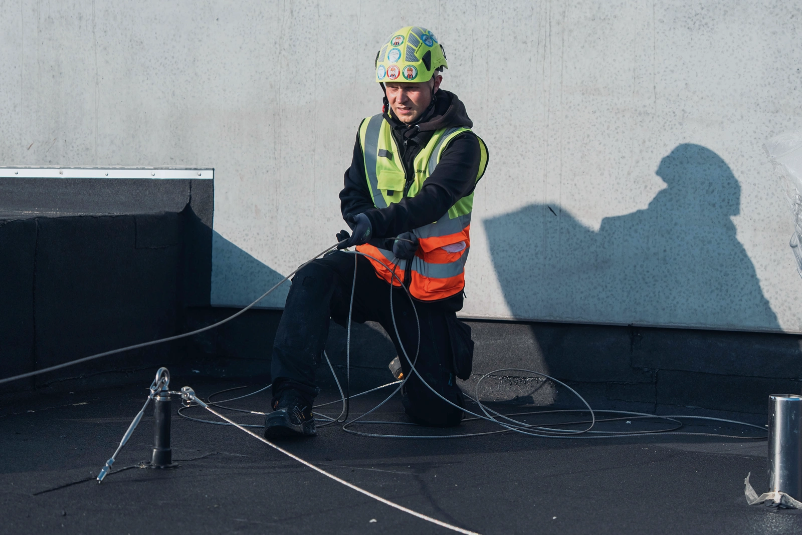 Montør arbejder med wirebaseret faldsikringssystem på fladt tag og tilpasser wiren mellem ankerpunkter.