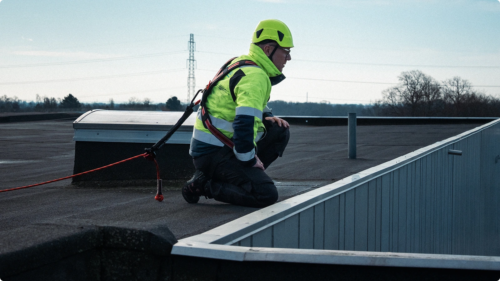 Medarbejder sikret med faldsikringssele og line under arbejde på fladt tag