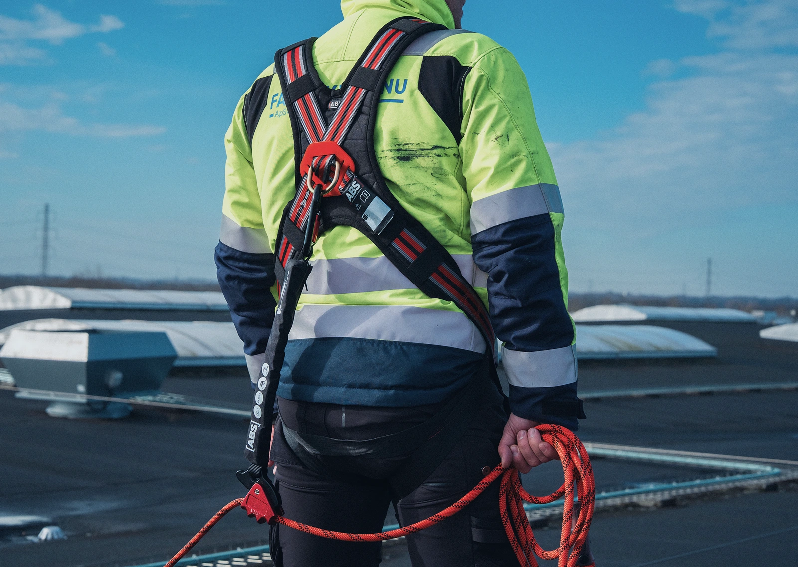 Medarbejder med sikkerhedssele og faldsikringsline under arbejde på fladt tag